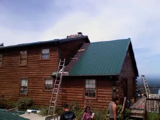 Green metal roof going on a two story log home with ladders set in Copalis Beach