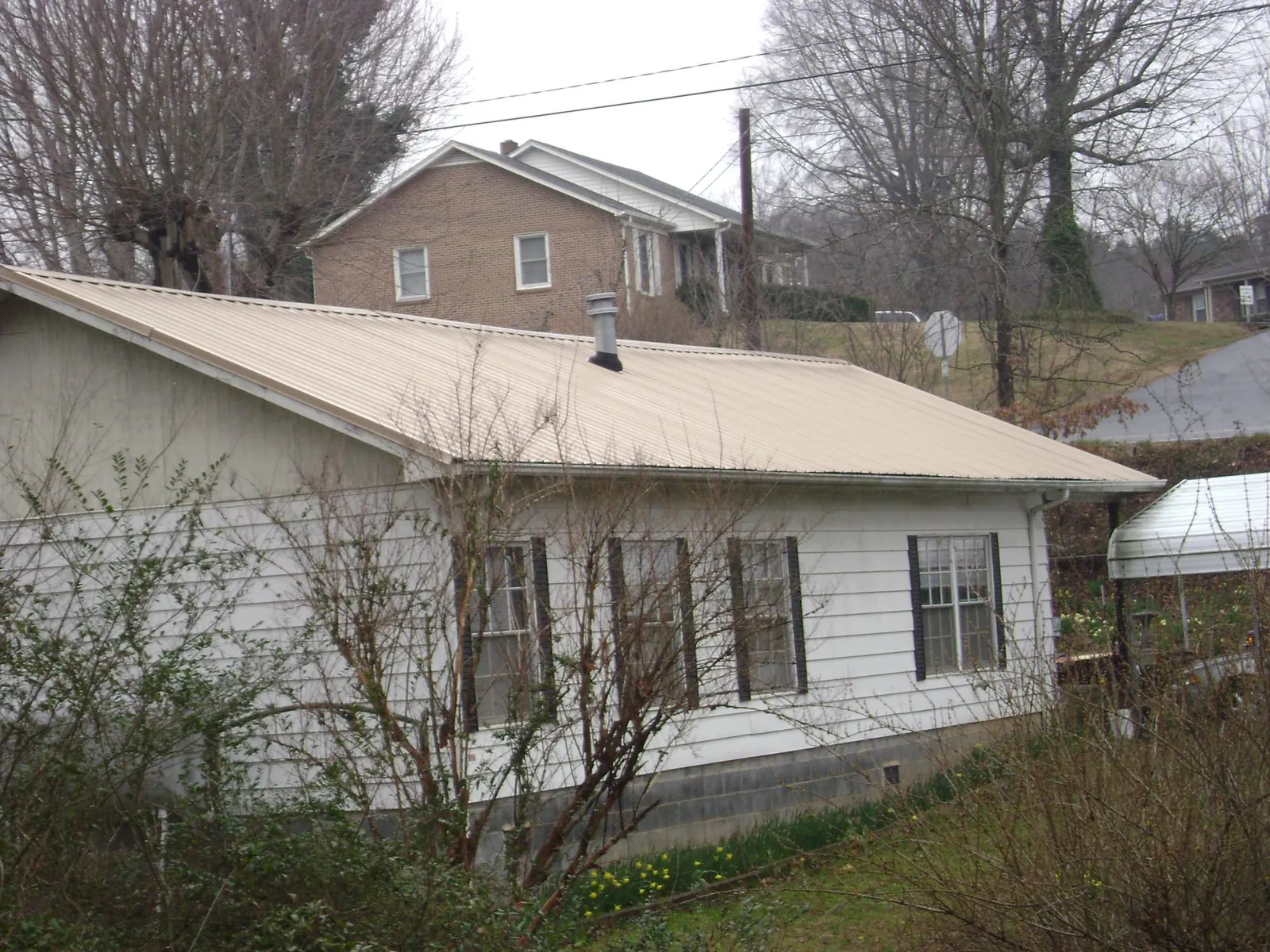 Tan metal roof on a white sided house set into a hillside — Commercial Roofing by Roofing Brothers in Copalis Beach